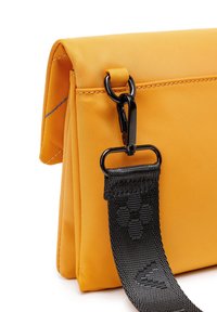 Žlutá látková taška s texturovaným černým popruhem. Obsahuje klopový uzávěr a kovovou sponu, která ukazuje kontrastní barvy a materiály.