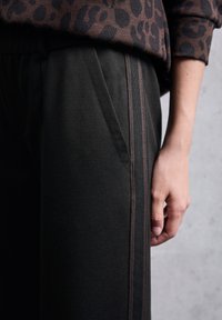Pantaloni neri a trama con tasche laterali, dotati di una sottile striscia a contrasto lungo la cucitura esterna e una vita rilassata.