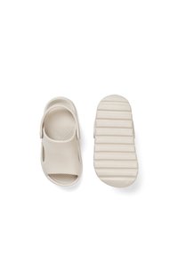 Beige Gleit-Sandalen aus Gummi, mit offenen Zehen, seitlichen Ausschnitten und einer strukturierten geriffelten Sohle für Grip und Komfort.