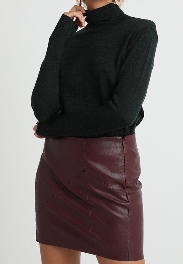 Dunkelgrüner Rollkragenpullover mit langen Ärmeln, kombiniert mit einem burgunderfarbenen Leder-Minirock, der diagonale Nahtdetails und einen Reißverschluss hat.