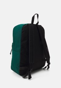 Sac à dos avec un design noir et bleu canard, présentant des bretelles réglables, une poignée supérieure et une texture de tissu lisse. Détails de poche latérale visibles.