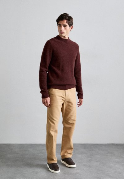 Burgundy wool sweater with a high neckline, paired with tan cotton pants and dark sneakers. Simple design, textured fabric, relaxed fit.