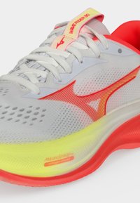 Άσπρο και κόκκινο παπούτσι τρεξίματος Mizuno Wave Rider 30 με κίτρινη σόλα και λευκά κορδόνια σε μονόχρωμο φόντο.