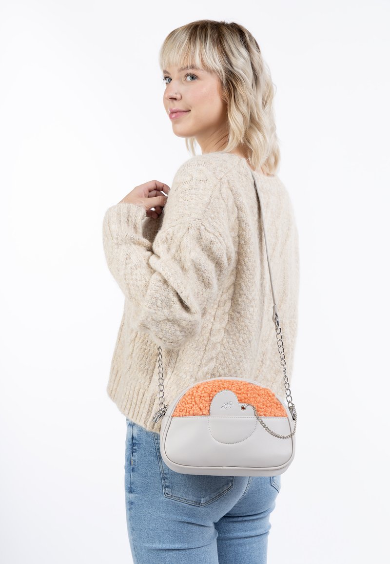 Borsa grigia con una parte superiore arancione a trama, forma arrotondata e tracolla in catena argentata, portata a spalla su uno sfondo neutro.
