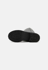 Semelle de botte en caoutchouc noir avec des motifs de creux profonds et des crampons hexagonaux. Bords renforcés et une partie supérieure lisse, légèrement texturée.