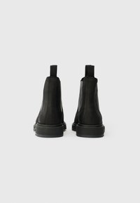 Bottines Chelsea en cuir noir avec un design élégant, une forme courbée, des panneaux latéraux en élastique et des languettes en boucle à l'arrière. Semelles en caoutchouc.
