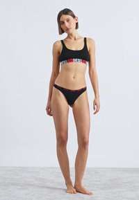 Mustast bralettist ja bikiinidest komplekt, millel on punase ja valge "DIESEL" logoga vöökumm; pehme kangas, sile tekstuur, kitsas lõige.