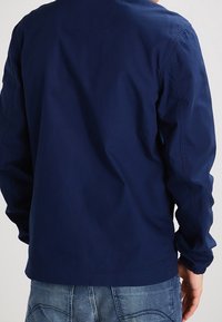 Giacca blu navy a maniche lunghe, realizzata in tessuto leggero. Presenta un design semplice e una vestibilità comoda, senza accenti o motivi visibili.