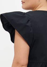 Black dress featuring flared short sleeves, lightweight fabric, and gathered detailing at the waist. Sleek and fitted design.