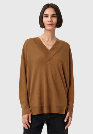 Pull en tricot marron avec col en V, manches longues et fentes sur les côtés. Doté d'un col texturé et d'un tissu doux. Porté sur un pantalon noir.