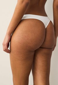 String blanc en tissu doux, avec un design taille basse offrant une couverture minimale et de délicats détails de couture.