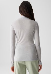 Langärmliges, hellgraues Oberteil aus einem weichen Stoff. Hat ein tailliertes Design und einen runden Halsausschnitt, kombiniert mit grünen Cordhosen.