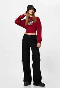 Rode cropped sweatshirt met een grafische print, gecombineerd met zwarte cargo pants met zijzakken en een relaxte pasvorm. Zwarte bucket hat en chunky laarzen.