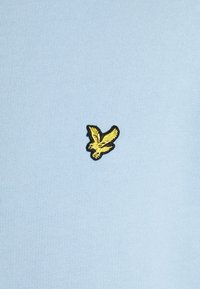 Petit oiseau jaune brodé avec contour noir sur un fond en tissu bleu clair.