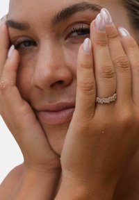 Ring mit einem Cluster aus klaren, rechteckigen Steinen, die in einem dünnen Goldeinfassung gesetzt sind. Die Hände des Modells ruhen sanft auf ihrem Gesicht.