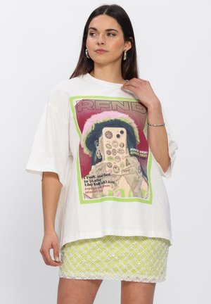 Vrouw met lang donker haar draagt een oversized wit T-shirt met kleurrijke afbeelding en een korte groene rok met wit rasterpatroon.