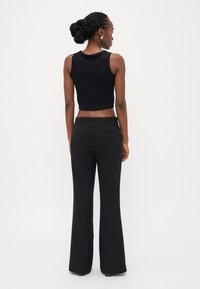 Svart kort topp och svarta utsvängda byxor, båda med en mjuk textur. Outfiten har inga mönster eller synliga detaljer av hårdvara.