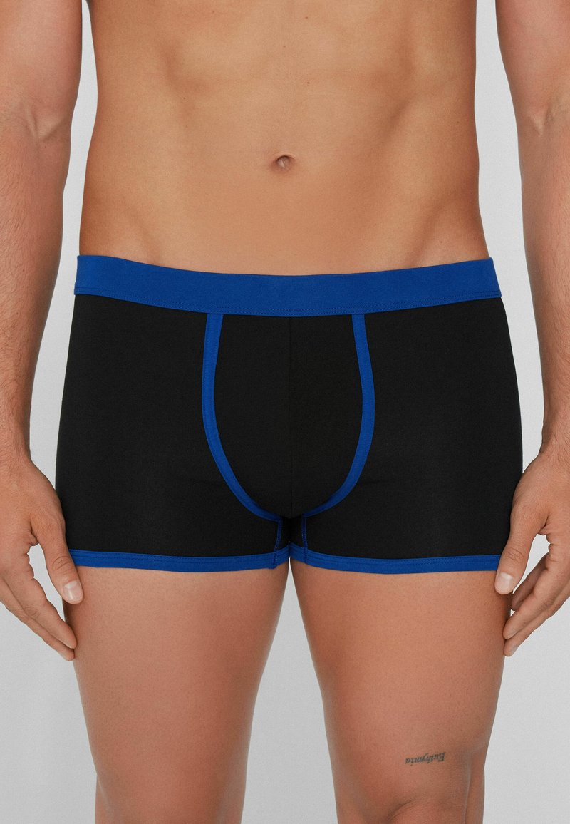 Boxers ajustados negros con una cinturilla elástica azul, con costuras en contraste y un diseño ceñido. Tela suave y lisa, de longitud media en el muslo.