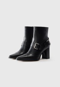 Botas de cuero negro hasta el tobillo con punteras puntiagudas, tacones cuadradores, cremallera lateral y correas anchas con hebillas de plata en cada zapato.
