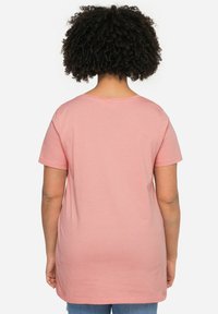 Camiseta rosa de manga corta con escote redondo, hecha de una tela suave, diseñada en un corte holgado, con un dobladillo trasero alargado.