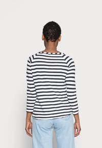 Chemise à manches longues rayée noir et blanc avec un col rond et une coupe décontractée, associée à un jean bleu clair. Matière en coton.