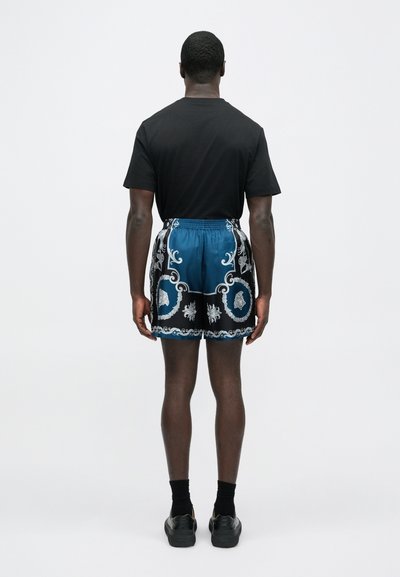 Completo da uomo con t-shirt nera e pantaloncini blu con intricati motivi argento, vita elastica e tessuto dalla texture liscia.