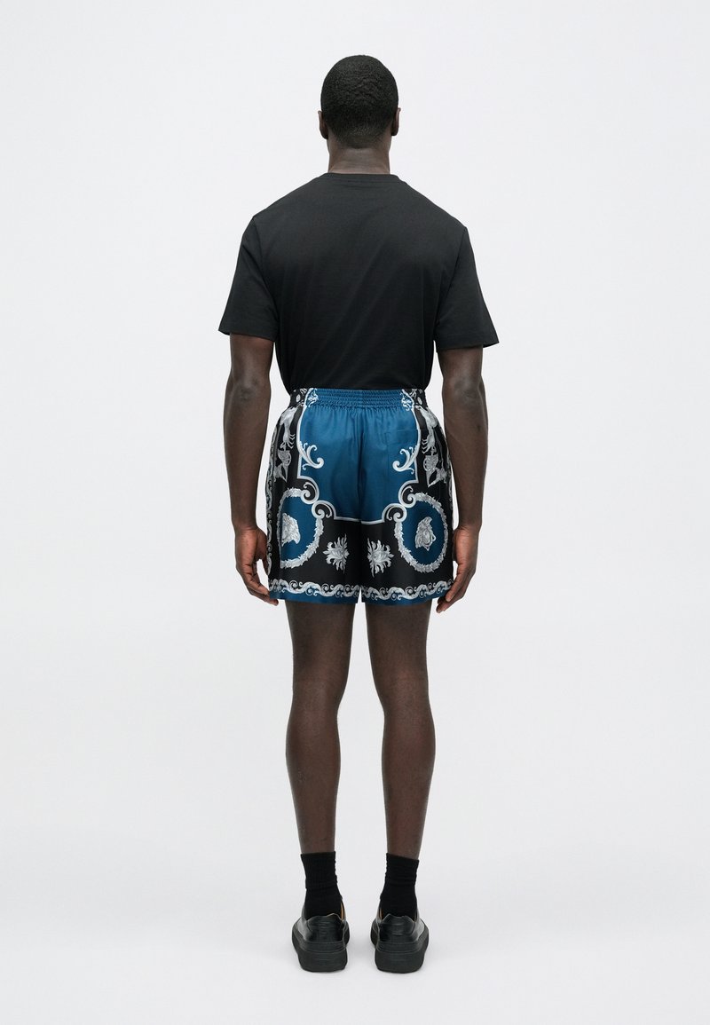 Herreoutfit bestående af en sort t-shirt og blå shorts med indviklede sølvmønstre, elastisk talje og en glat stoftekstur.