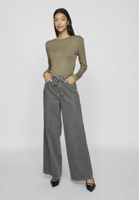 Olivgrön långärmad topp som kombineras med högmidjade, vida grå jeans med dragsko i midjan. Svarta pumps med smal tå fulländar outfiten.