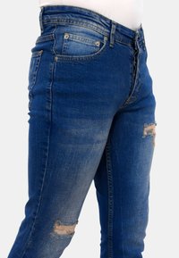 Donkerblauwe denim jeans met een slim fit, voorzien van versleten kniedetails en een traditioneel zakontwerp. Glad textuur met lichte vervaging.