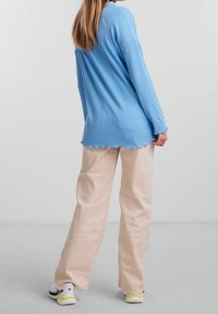 Ljusblå ribbad långärmad topp med rundad nederkant, i kombination med beiga vida byxor. Bekväma sneakers med neondetaljer fulländar looken.