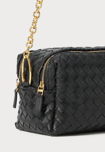 Borsa a mano in pelle nera con texture intrecciata, hardware dorato, due scomparti con zip e una tracolla a catena per il trasporto.