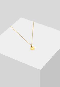 Guld vedhængsarmbånd med en rund charm, der har en struktureret overflade, fastgjort til en fin kæde, præsenteret på en lys grå geometrisk baggrund.