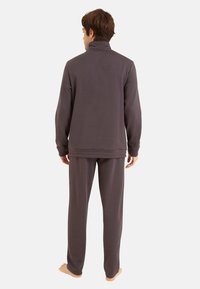 Ensemble de détente en polaire gris comprenant une veste à col haut et un pantalon assorti. Le matériau semble doux et confortable, avec une coupe décontractée.