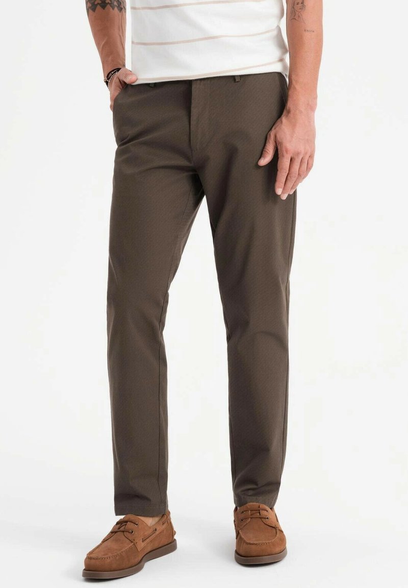 Pantaloni marroni realizzati in tessuto testurizzato, con un design slim fit, abbinati a scarpe in pelle marrone. Linee pulite e accenti sottili.