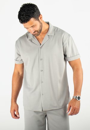 Chemise à boutons à manches courtes gris clair en tissu texturé, avec un col camp et des manches retroussées, associée à un pantalon assorti.