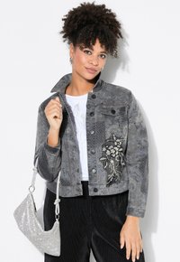 Grå denimjacka med blommönsterbroderi, nitar, knappstängning och falsk krage; matchad med en handväska i silverpärlor.