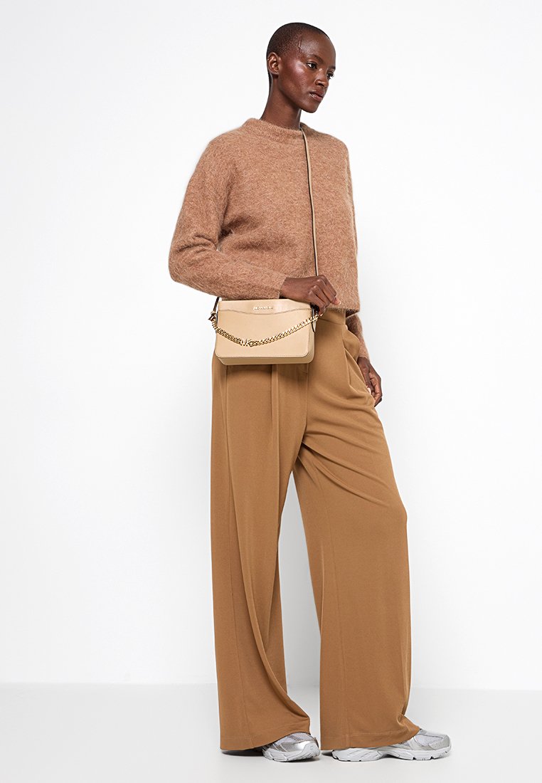 Beige schoudertas met een kettingband, gecombineerd met een roestkleurige fuzzy trui en brede beige broek. Zilveren sneakers maken de outfit compleet.