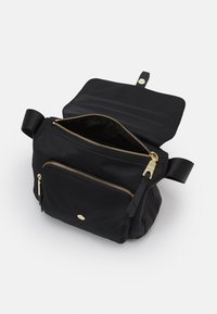 Černá nylonová crossbody taška se zlatými zipy, přední kapsou a klopou se zacvakávacím uzávěrem, vystavená otevřená na bílém pozadí.