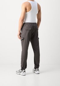 Grå cargobyxor med elastiska muddar och fickor, tillverkade av lättviktsmaterial. I kombination med en vit tanktop och grå sneakers.