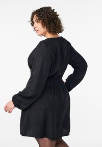 Melna kleita ar teksturētu audumu, garām pūkainām piedurknēm un elastīgu vidukļa jostu, ar brīvu piegriezumu un vieglu uzplaiksnījumu.