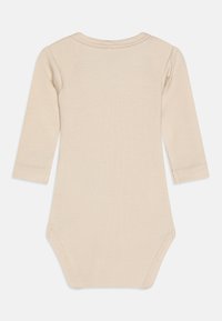 Kreminės spalvos ilgomis rankovėmis kūdikio bodžiukas iš riboto audinio, suapvalintu iškirpimu ir spaudėmis apatiniame krašte. Lygus, minkštas tekstūra.