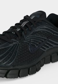 Μαύρο αθλητικό παπούτσι Nike με υφή από δίχτυ σε σχήμα κυψελών, γυαλιστερό λογότυπο Swoosh, αντανακλαστική λωρίδα στα κορδόνια και τμηματική ενισχυμένη σόλα.