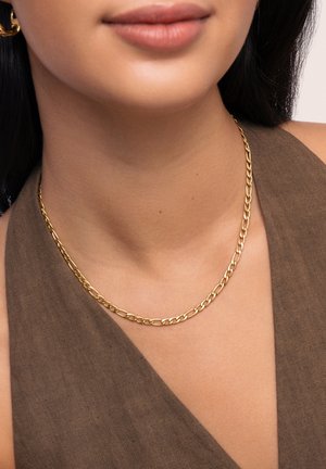 Collier en chaîne en or avec des maillons ovales entrelacés, reposant sur un cou bronzé, sur fond de tissu marron.