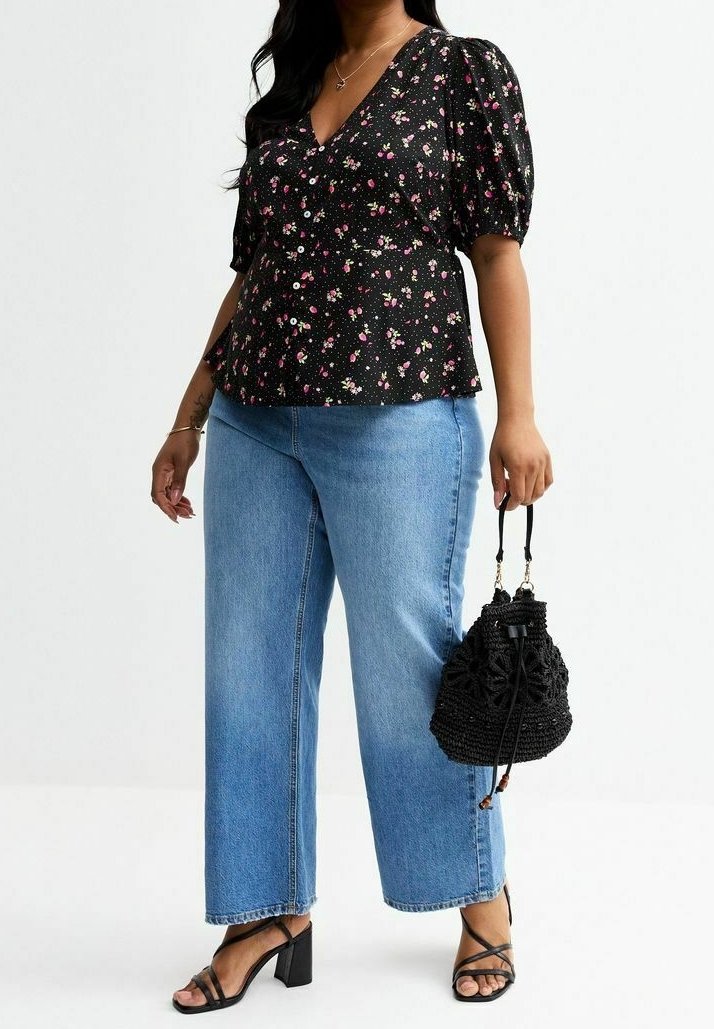 Femme portant un chemisier noir à manches bouffantes à motif floral, un jean bleu clair, des sandales noires à talons et tenant un sac à main noir tissé.