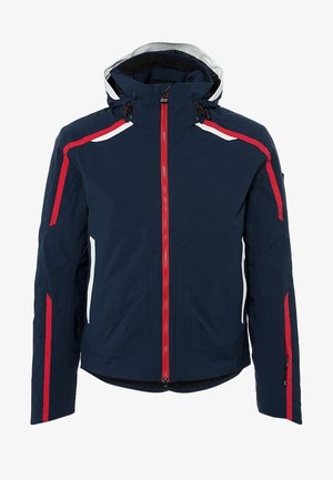 Man draagt een marineblauwe skijas met rode en witte strepen, een grijze coltrui, zwarte sneeuwbroek en zwarte skischoenen met rode zolen.
