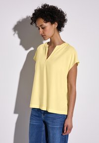Maglietta gialla a maniche corte con scollatura a V e vestibilità ampia, abbinata a jeans in denim blu. Tessuto morbido e design semplice.