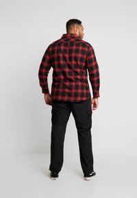 Rot und schwarz karierter Flanellhemd mit langen Ärmeln, kombiniert mit schwarzen Cargo-Shorts. Beide Kleidungsstücke sind locker geschnitten und haben ein lässiges Design.