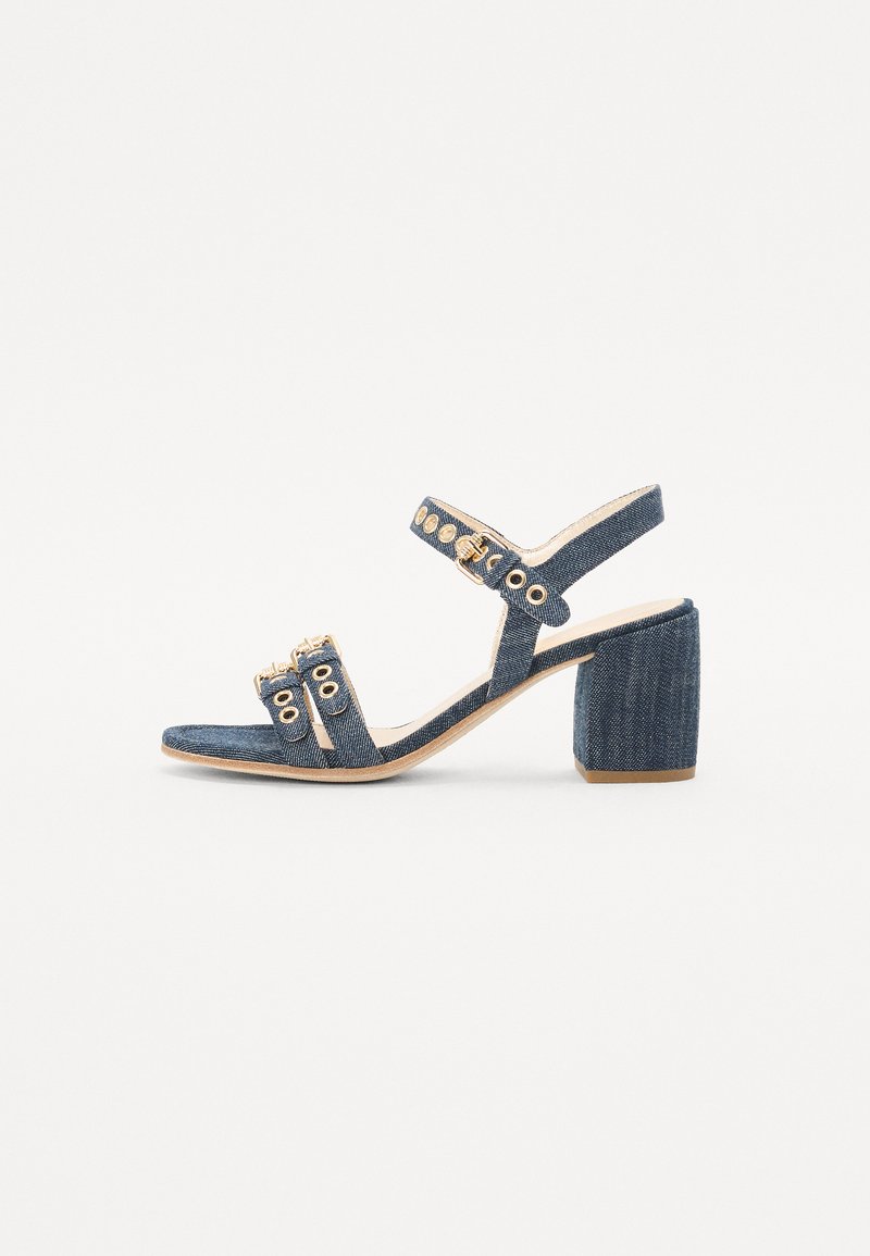 Denim høyhælte sandal med blokkheel, åpen tå og ankelstroppe. Har gullfarget detaljer og flere øyeletsdekorasjoner.