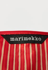 Κόκκινο ύφασμα με κάθετες ρίγες σε διάφορα πλάτη· εμφανίζει μια μαύρη ετικέτα με την ένδειξη «marimekko» σε λευκό γράμμα στην κορυφή. Ορατή λεπτομέρεια φερμουάρ.
