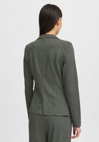 Juodai ir kreminiai houndstooth rašto švarkai, prigludęs dizainas su įpjautu apykakle ir ilgomis rankovėmis, tekstūra atrodo lygi ir pritaikyta.